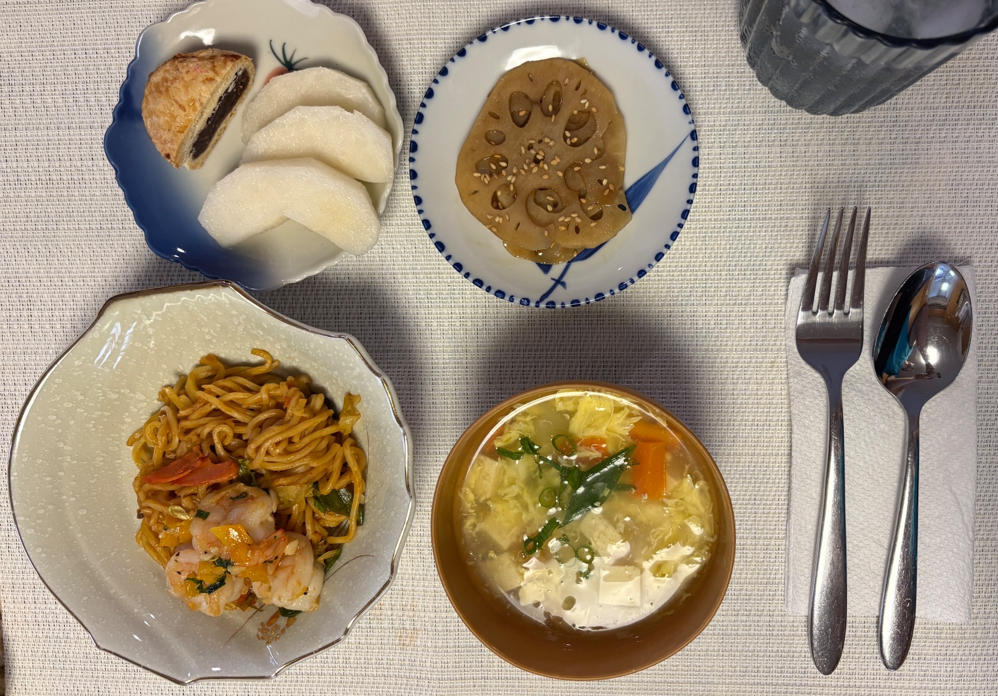 Noodles, soup, lotus root, and fruit served at a place setting